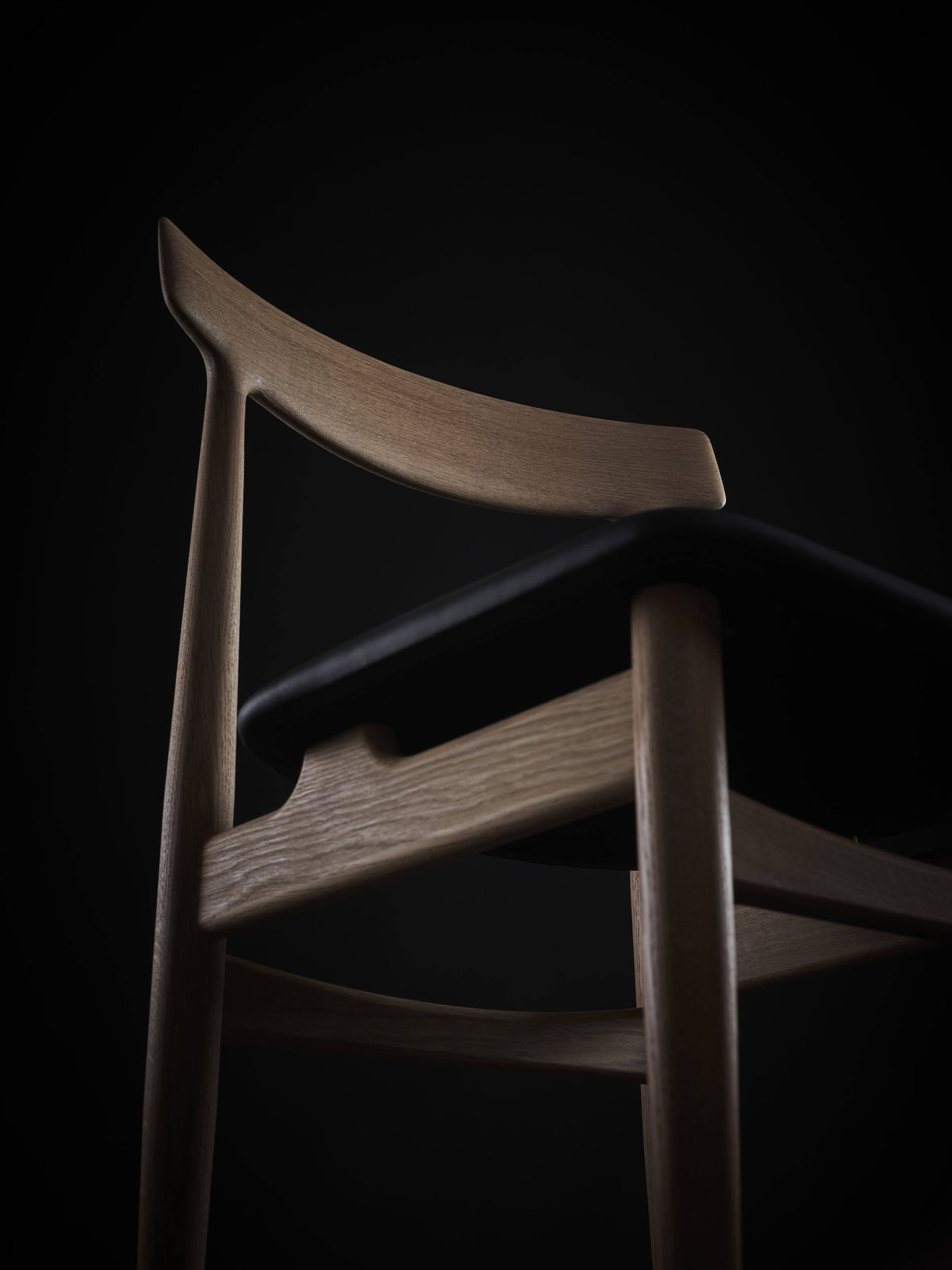 Low-angle close-up of the light wood Eikund Hertug Dining Chair, showing the curved grain-patterned backrest, black seat edge, and rounded front leg joined to the side rail.