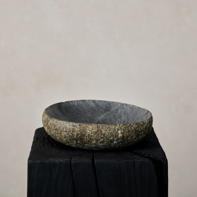 Natural stone bowl on a black stand against a beige background