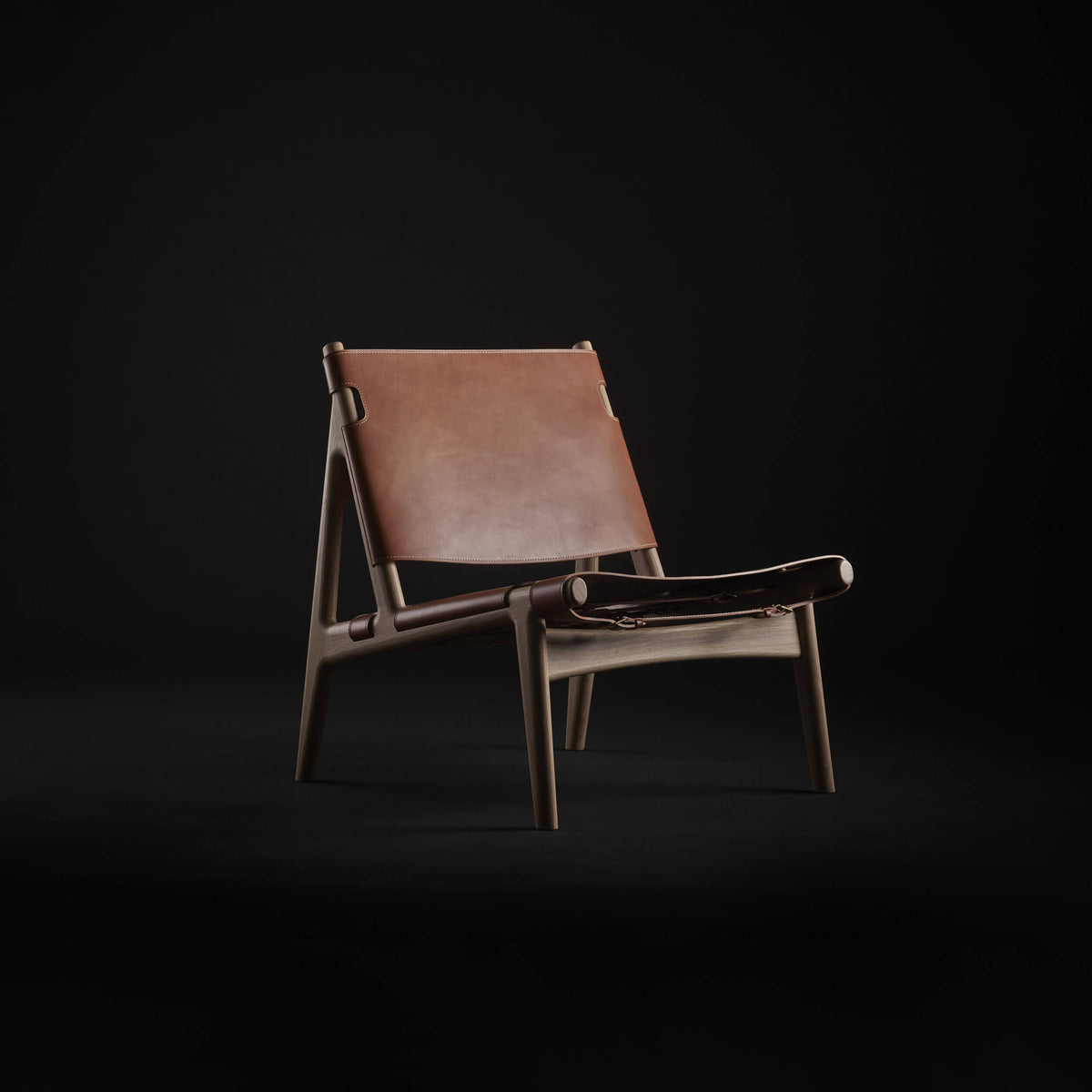 Three-quarter front view of the Eikund Hunter Lounge Chair in a dark studio, showing warm tan leather stretched across an angled wood frame with open sides and splayed legs.