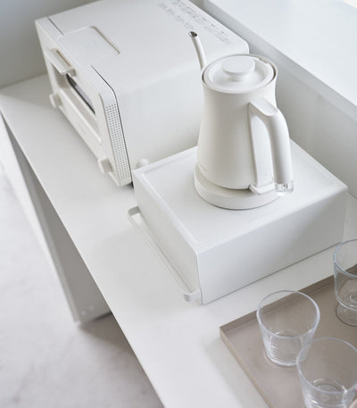 White electric kettle on a white surface with a white appliance in the background