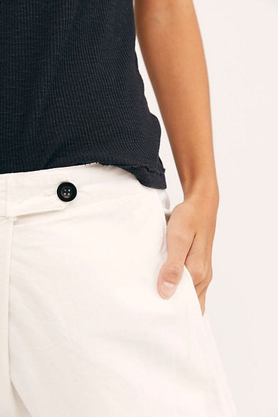 Close-up of the white Canvas Souk pants showing the black front button, waistband, and side pocket.