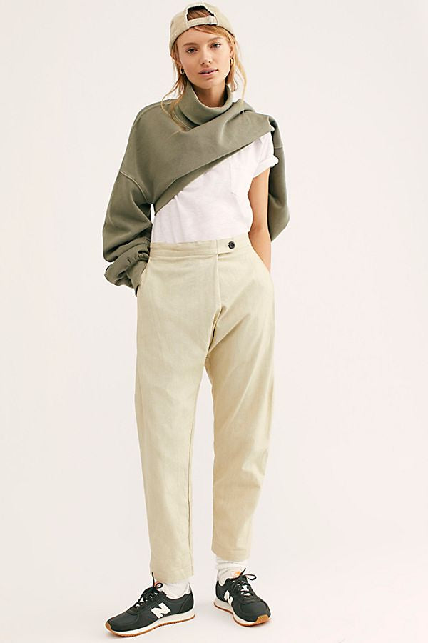 Model wearing natural cream Canvas Souk pants with a white T-shirt, olive sweatshirt draped over the shoulders, backward cap, and green sneakers.