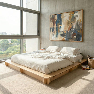 Studio Furnis wood bed platform with rumpled white bedding beside a large window and abstract artwork in a modern concrete bedroom