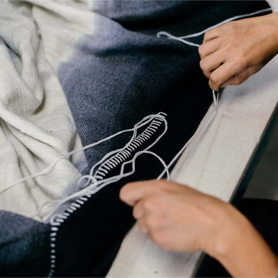 Detailed overhead view of hands forming the decorative white looped stitching along the throw’s dark border