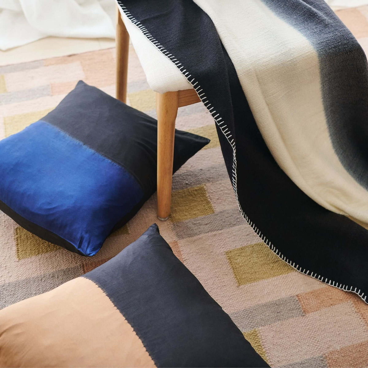 Ink Black and White throw draped over a wood chair above a geometric rug with blue, charcoal and tan floor cushions
