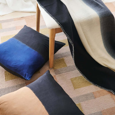 Ink Black and White throw draped over a wood chair above a geometric rug with blue, charcoal and tan floor cushions