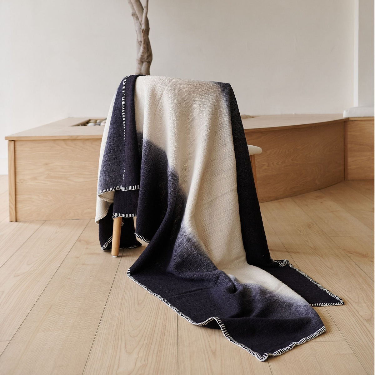 Ink Black and White merino throw draped over a wood chair in a minimalist room, showing its long color-block design and stitched border
