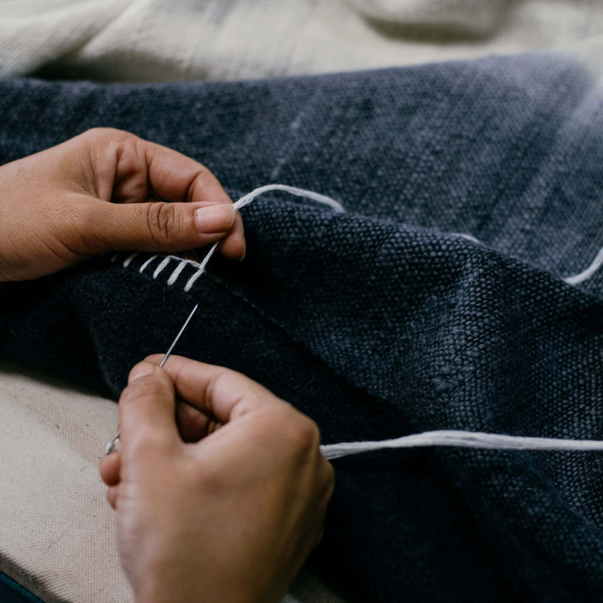 Close-up of an artisan hand-stitching the edge of the dark merino wool throw with contrasting white yarn
