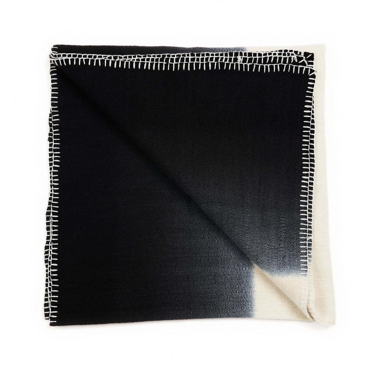 Folded Ink Black and White merino throw against a white background, showing a diagonal cream corner and hand-stitched border