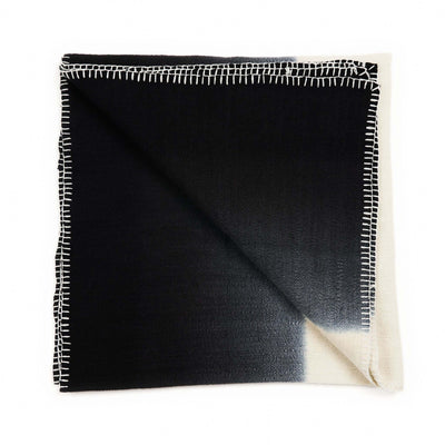 Folded Ink Black and White merino throw against a white background, showing a diagonal cream corner and hand-stitched border