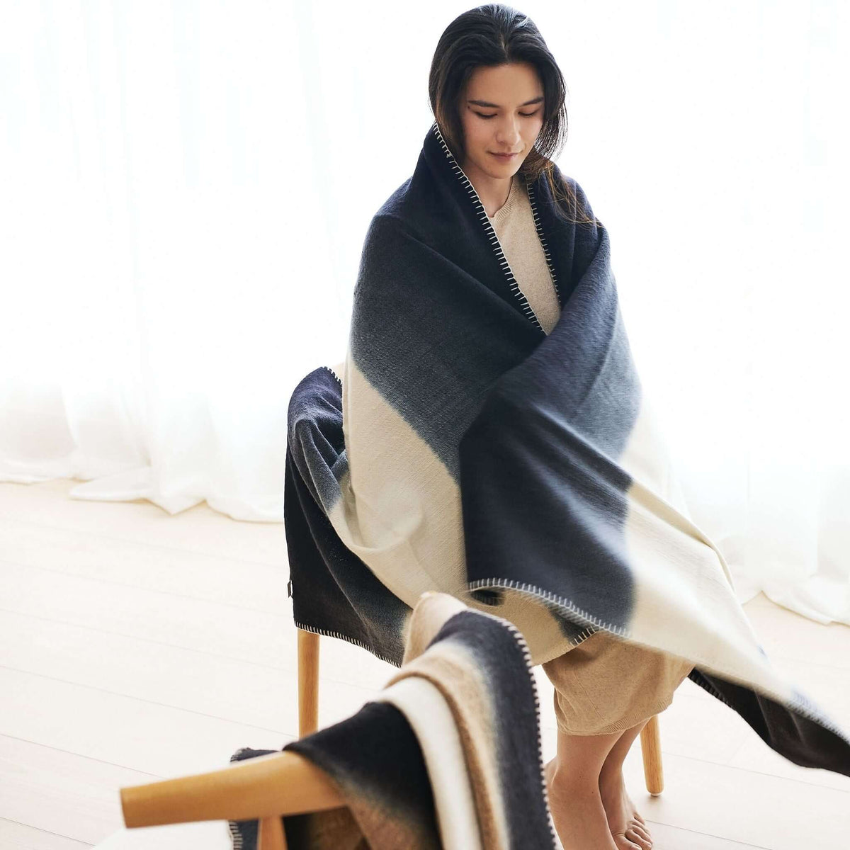 Woman wrapped in the Ink Black and White merino wool throw, displaying its generous size and broad contrasting panels