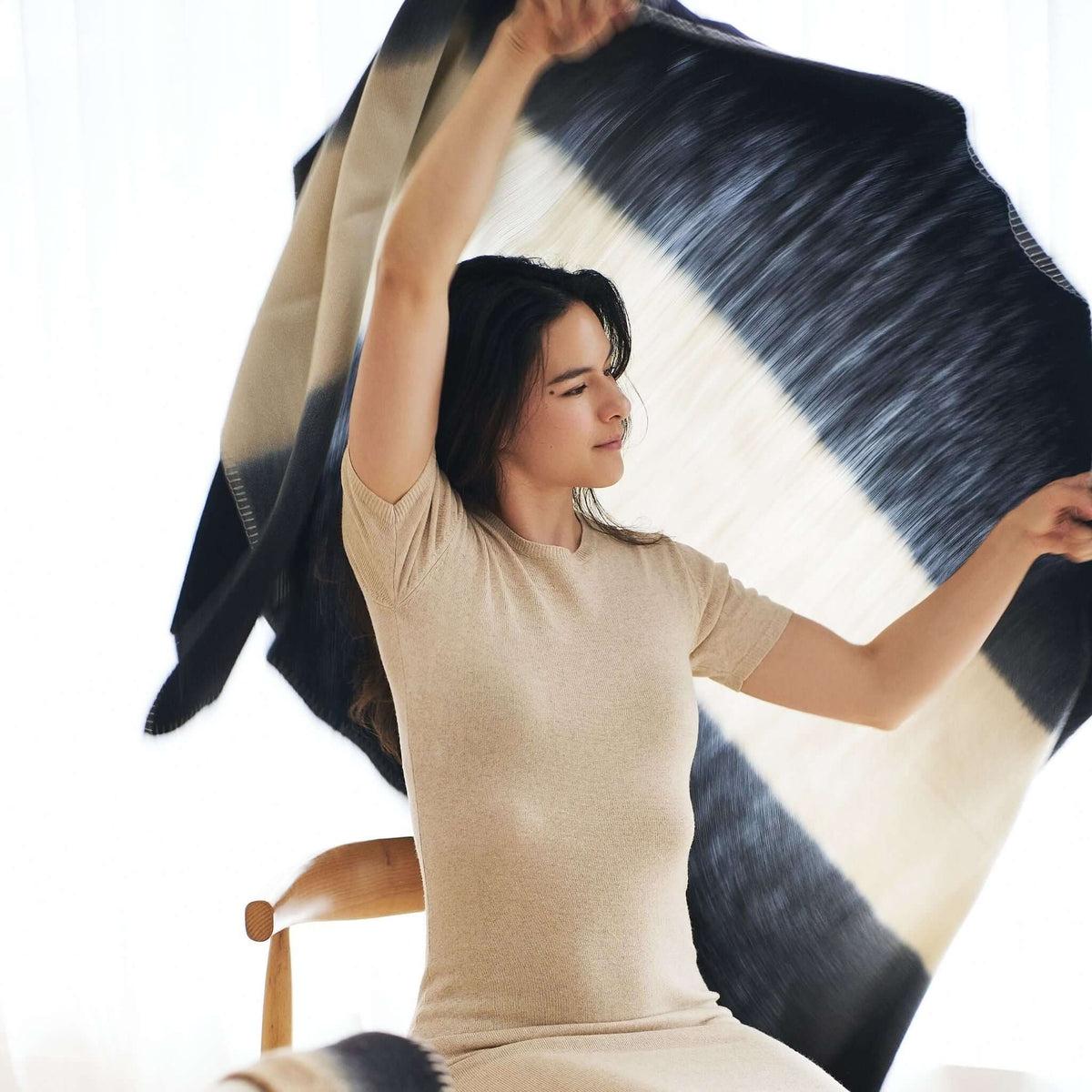 Woman holding the Ink Black and White merino throw fully open to display its large-scale black-and-cream color blocking