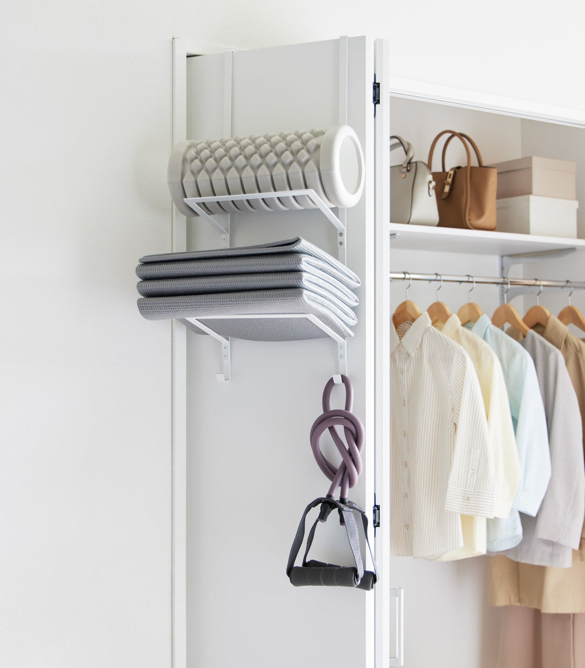 White Yamazaki Home Over-the-Door Fitness Equipment Hanger - Steel on a closet door, storing a grey foam roller, folded grey exercise mat and purple resistance bands with black handles.