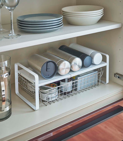 Kitchen shelf with storage rack holding tumblers and a basket, above a countertop.