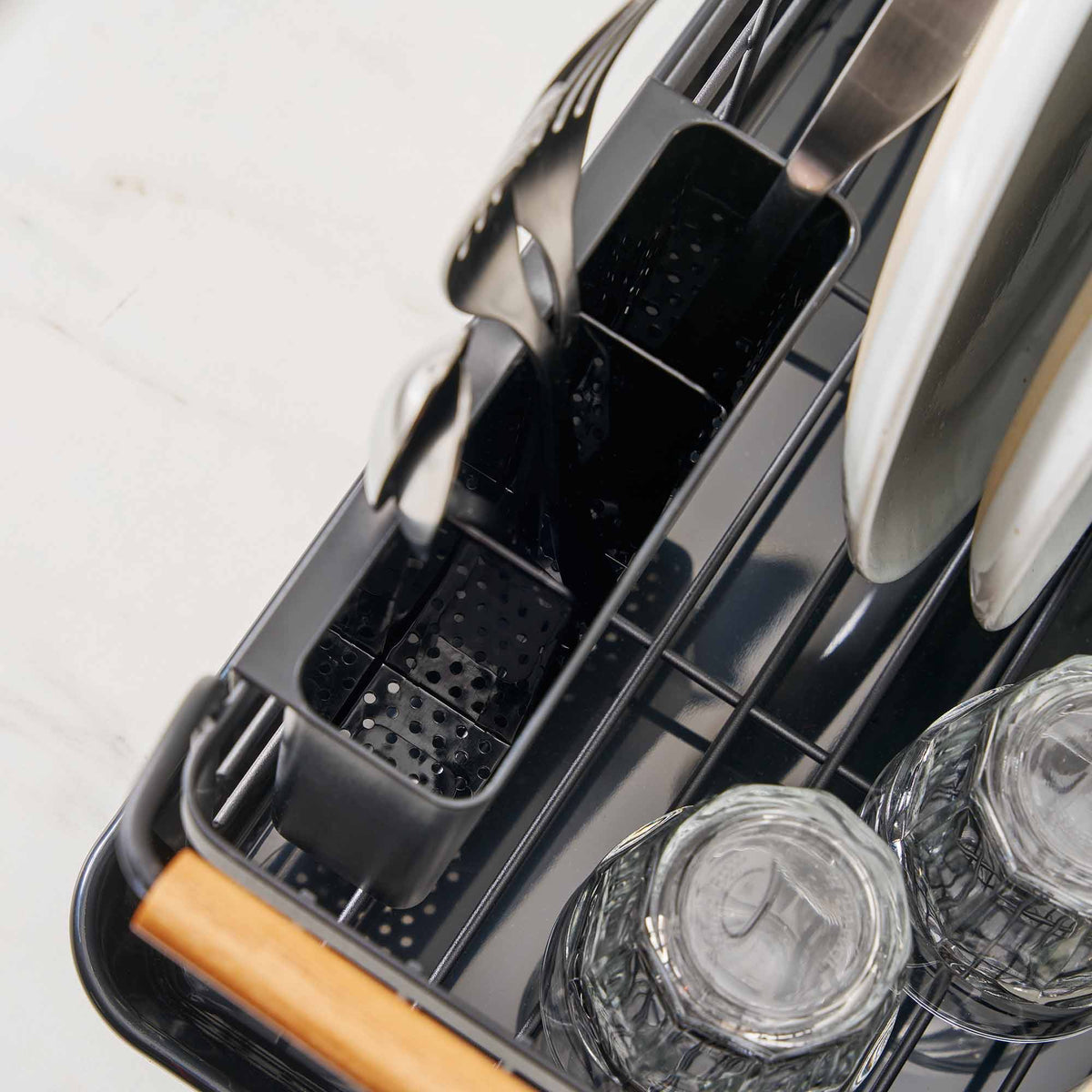 Overhead detail of the Yamazaki Home Dish Rack - Steel + Wood, revealing drainage holes in the divided utensil caddy, inverted glasses, wire dish supports and a light wood handle.