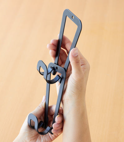 Close-up of two hands holding black Yamazaki Home Cascading Storage Hooks - Steel, showing how the elongated frames link together beside the projecting curved hooks.