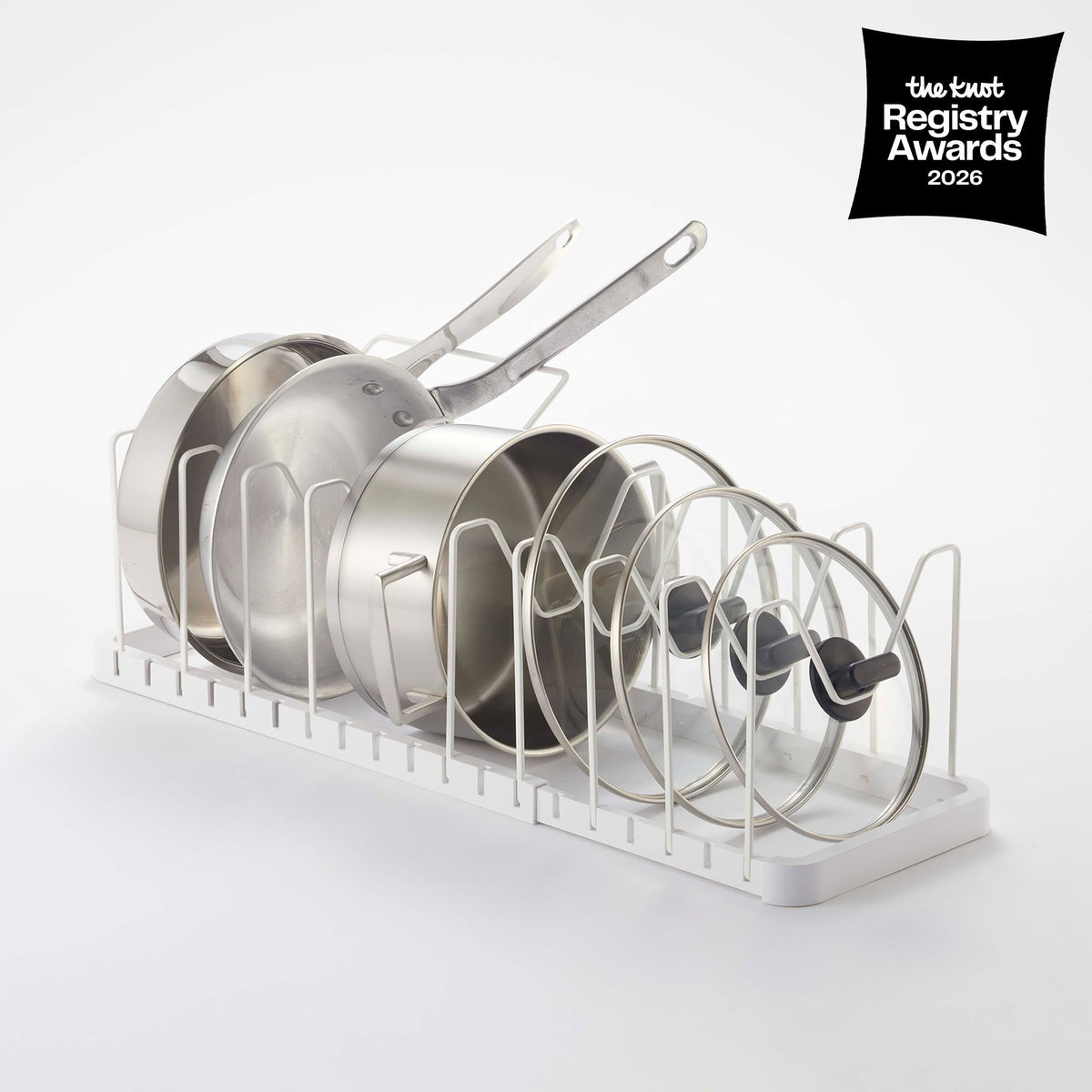 White Yamazaki Home Adjustable Pot Lid Organizer - Steel holding upright frying pans, saucepans and glass lids between wire dividers; a black badge reads The Knot Registry Awards 2026.
