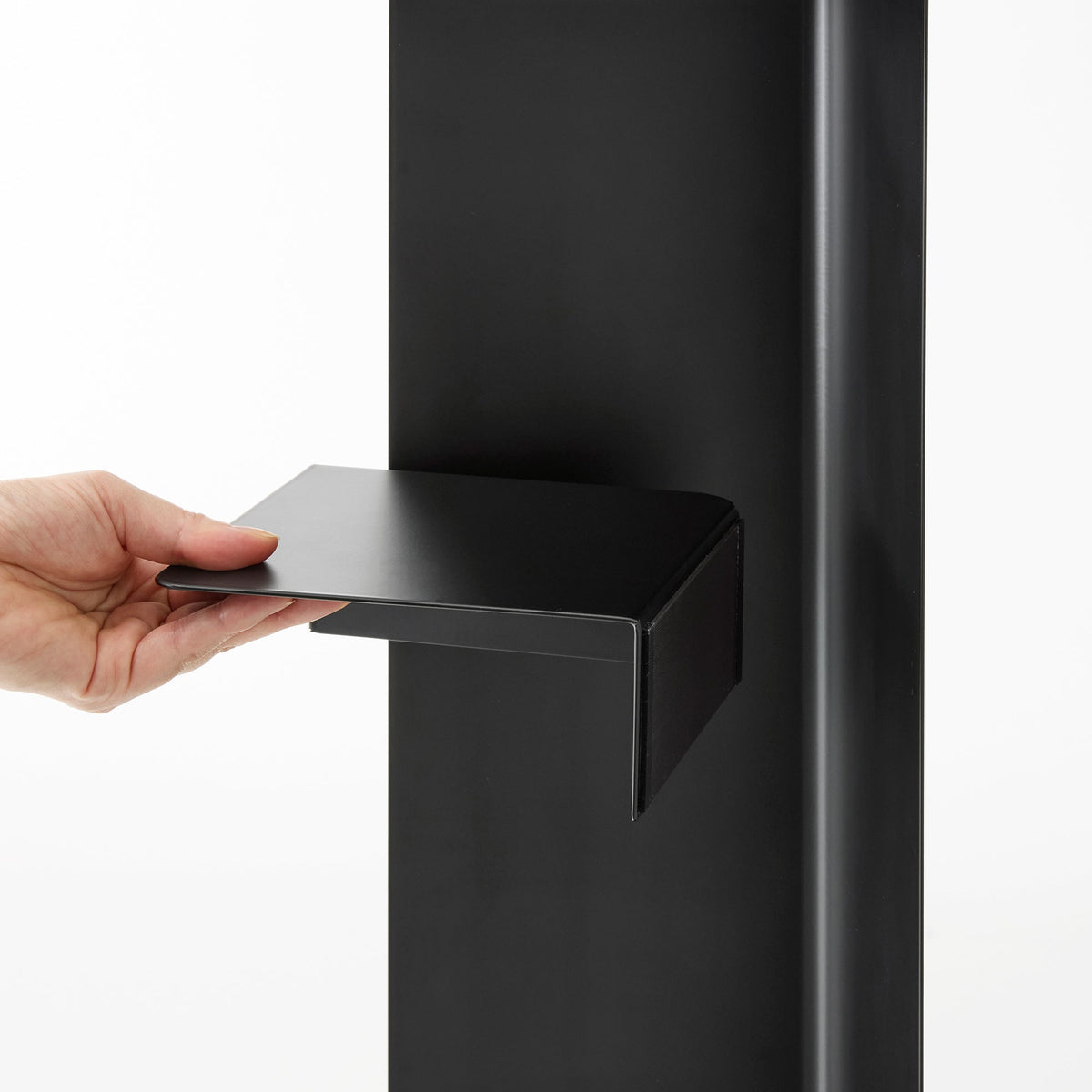 A hand holds the black shelf component of the Yamazaki Home Rolling Bathroom Organizer - Steel partly away from the panel, revealing its tray shape and folded side.