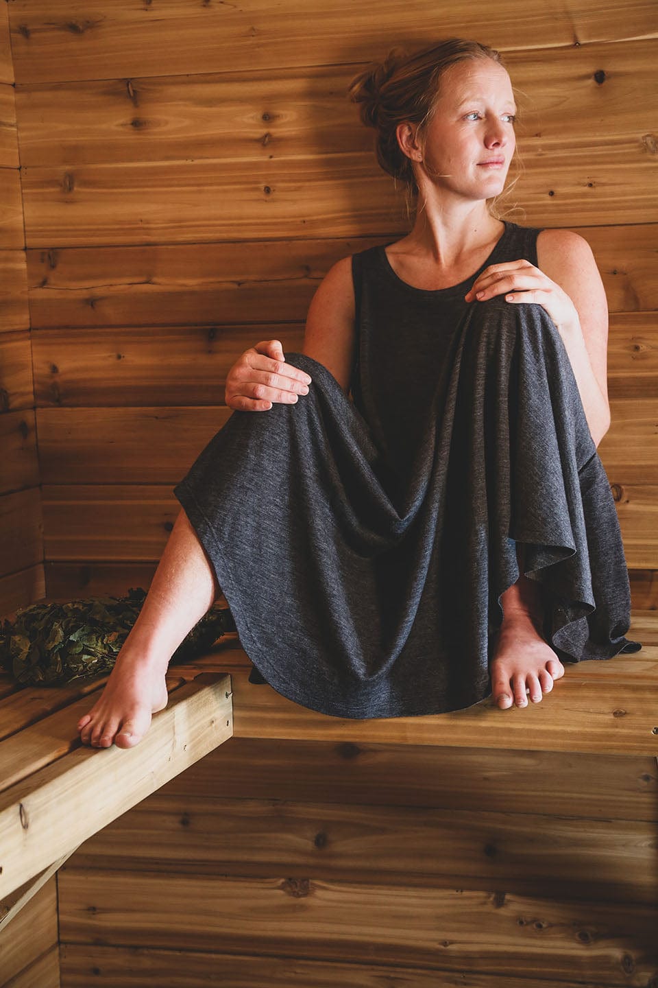 Woman wearing a merino wool sauna dress while relaxing on a traditional wooden sauna bench in Finland.