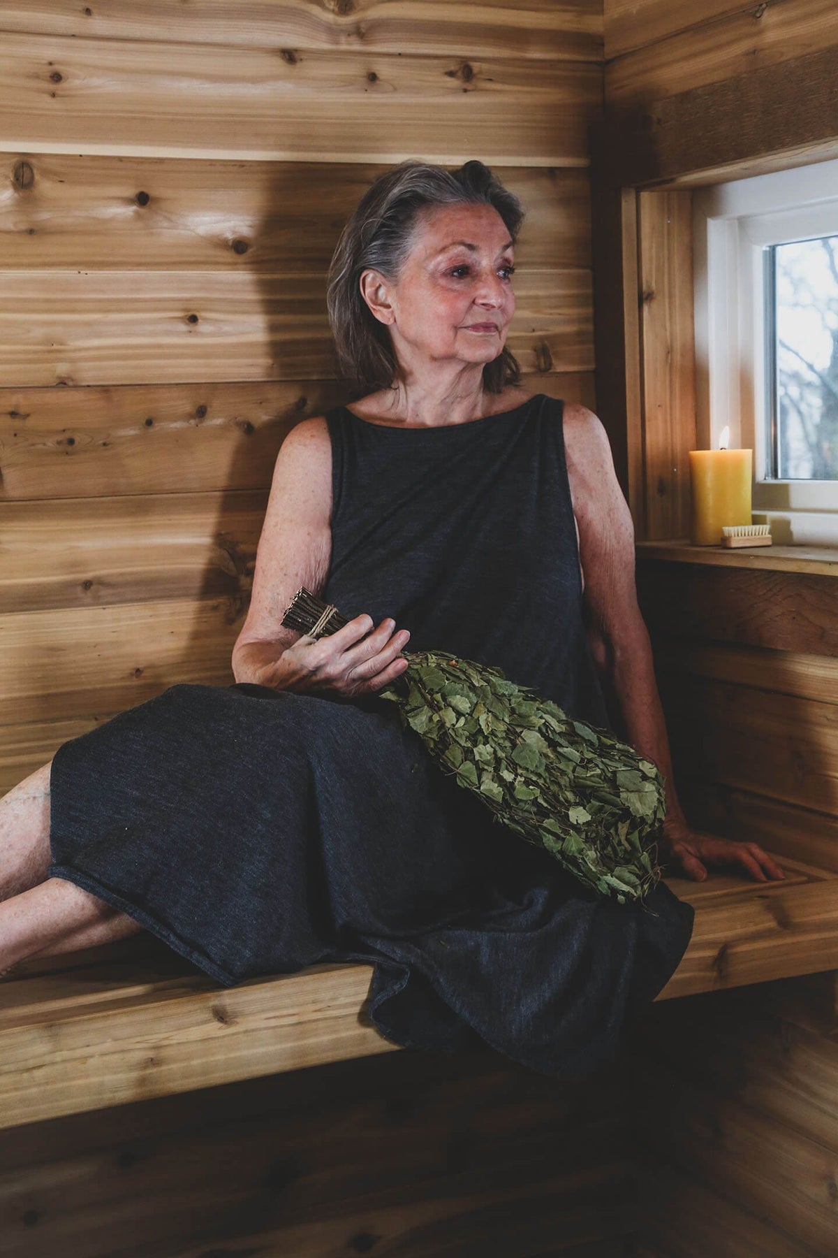 Merino wool sauna dress paired with fresh sauna greenery in a traditional wood sauna setting.