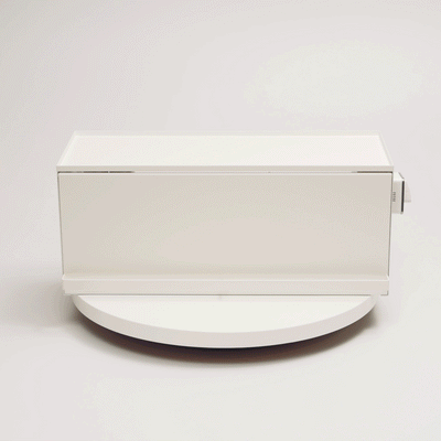 A hand demonstrates the white Yamazaki Home Open-Back Countertop Storage Rack - Steel on a round display platform, showing its open back, solid side panel and projecting front handle.