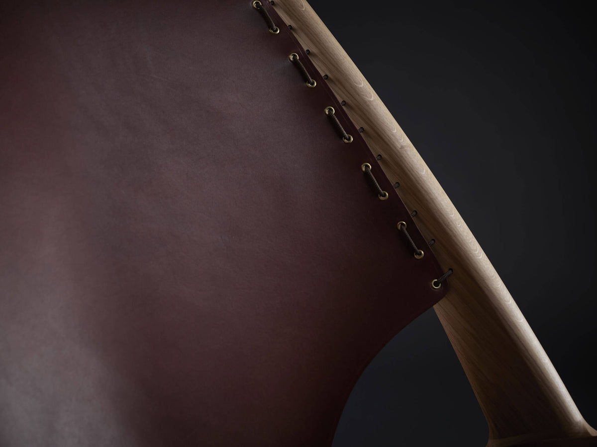 Close-up of the Eikund Krysset Lounge Chair’s reddish-brown leather back, showing its smooth surface and looped lacing along a light wood upright.