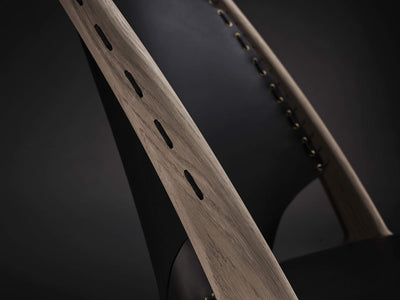 Close-up of the Eikund Krysset Lounge Chair’s light wood back upright, showing elongated lacing slots beside a black leather panel.