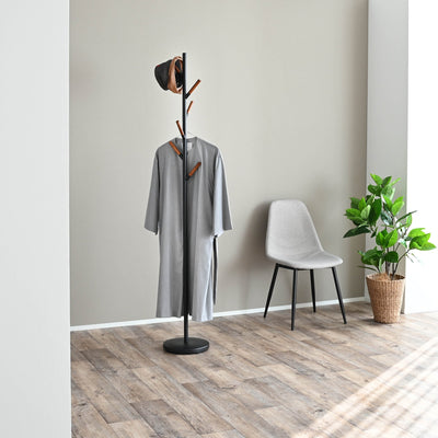 Black Yamazaki Home Coat Rack (70" H) - Steel holding a long grey coat and hat beside a grey chair and green potted plant on wood flooring.