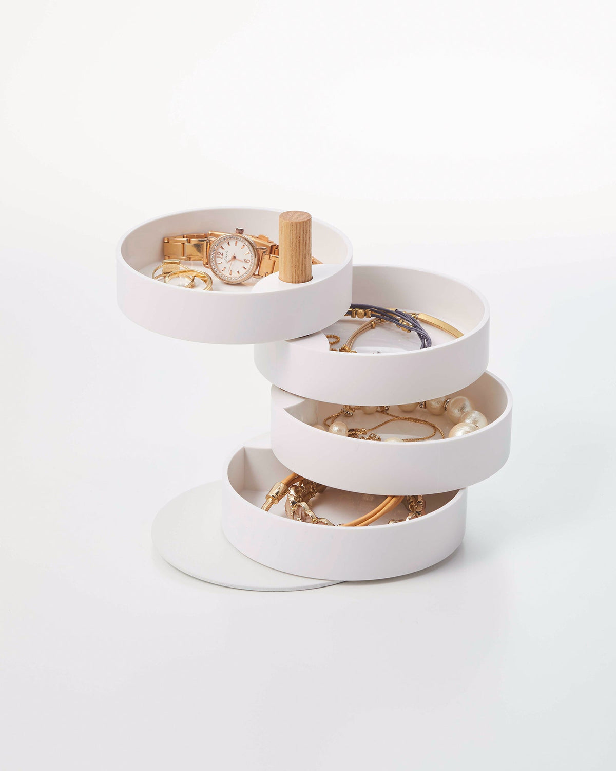 White Yamazaki Home Open Top Stacked Jewelry Organizer with four round trays swivelled apart around a light wood post, displaying a gold-toned watch, bracelets, necklaces and pearl-like jewellery on a pale background.