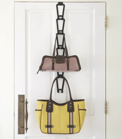 Black Yamazaki Home Cascading Storage Hooks - Steel on a white door, with several empty links above a patterned handbag and a large yellow tote hanging below.