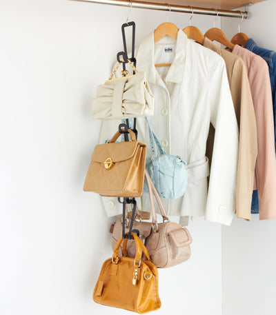 Black Yamazaki Home Cascading Storage Hooks - Steel storing cream, tan, light blue, beige and orange handbags vertically beside a row of pale clothing in a closet.