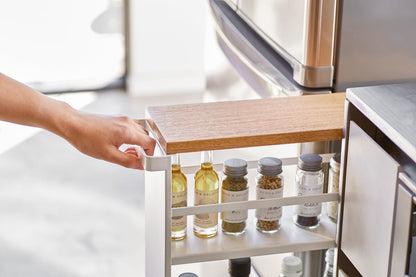 Kitchen drawer with spice rack and bottles, hand reaching in