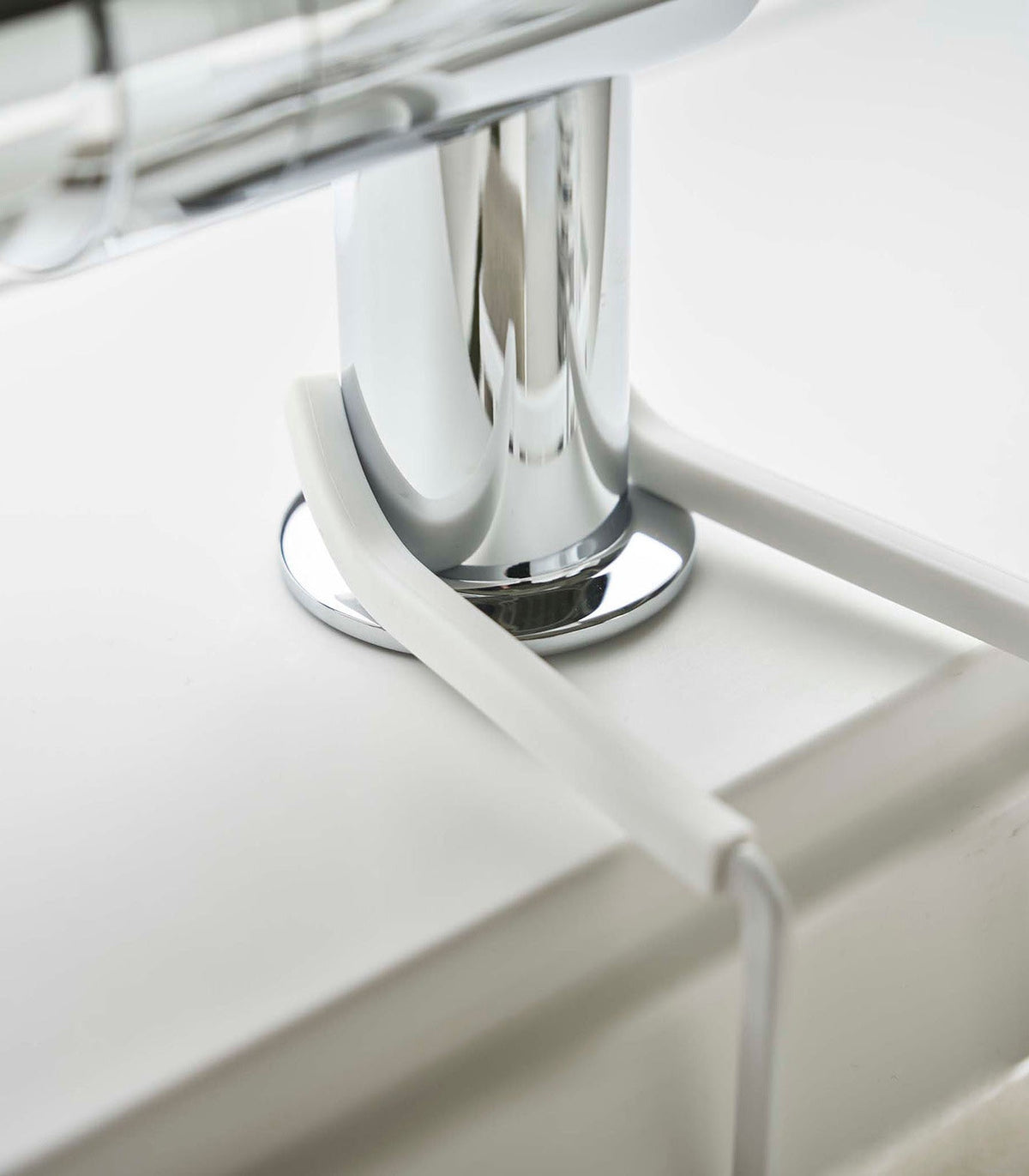 Detail of the white Yamazaki Home Faucet-Hanging Sponge Caddy - Steel support arms curving around the faucet base and bending down over the sink rim.