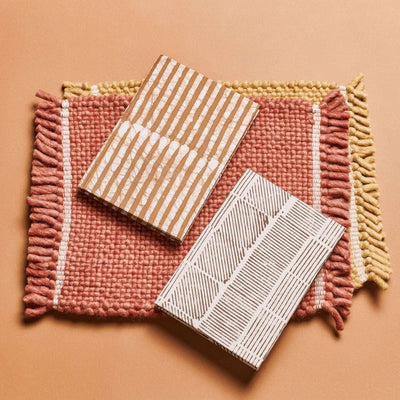 Oak Brown and white color variations of the handmade journal arranged on a rust-colored woven mat