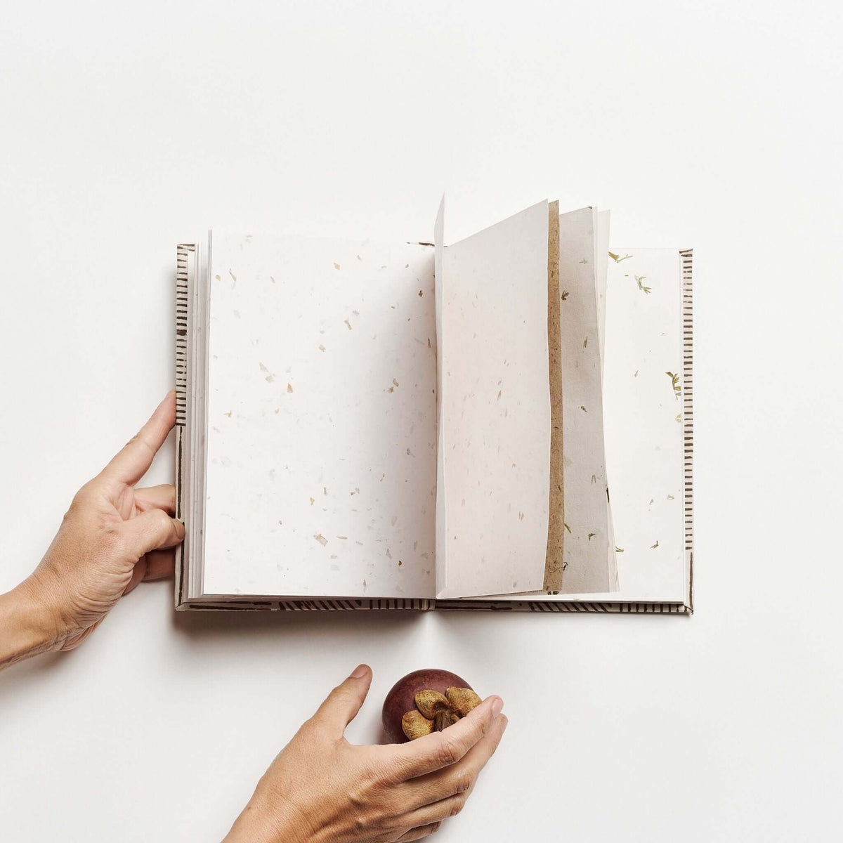 Open Oak Brown artisanal journal showing cream handmade pages with natural flecks as hands hold the book beside a cup