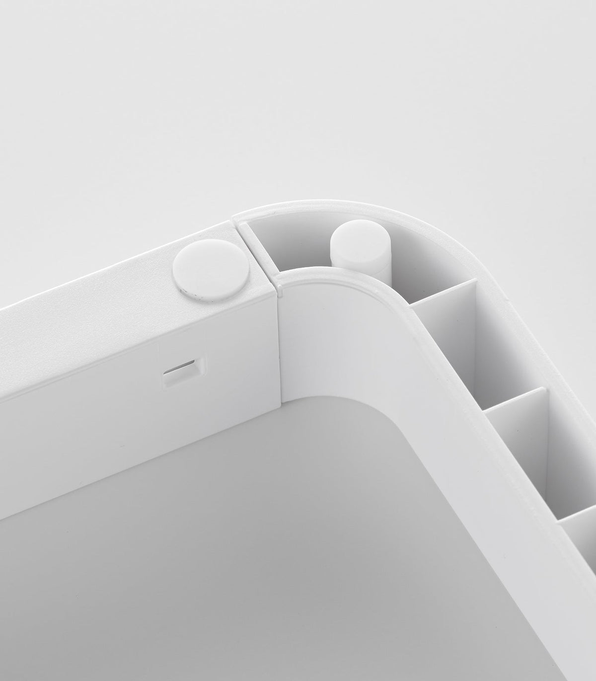 Detail of a rounded corner on the white Yamazaki Home Adjustable Pot Lid Organizer - Steel, revealing overlapping base sections and small circular fittings.