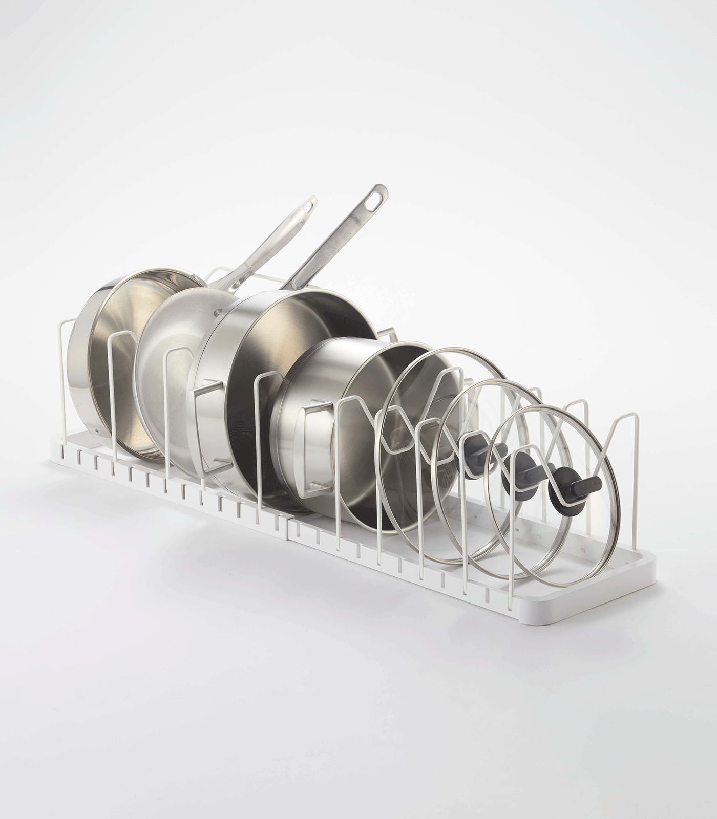 Angled view of the white Yamazaki Home Adjustable Pot Lid Organizer - Steel on a pale background, with cookware arranged from tall handled pans to smaller glass lids.
