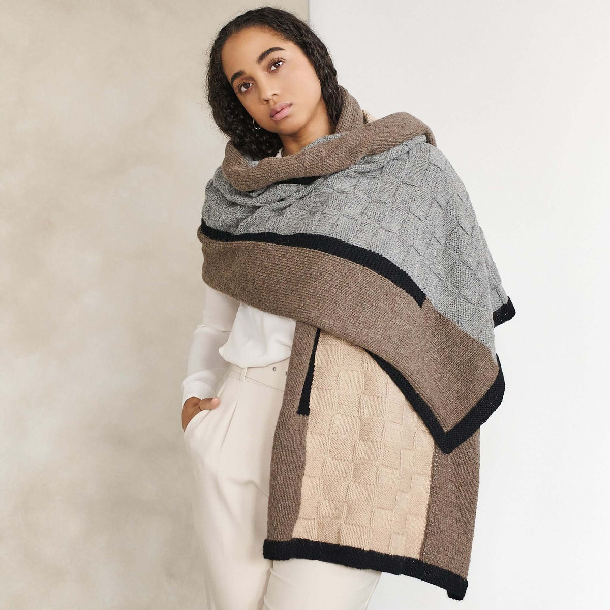 Woman wrapped in the oversized blanket shawl with gray and brown panels across her shoulders.