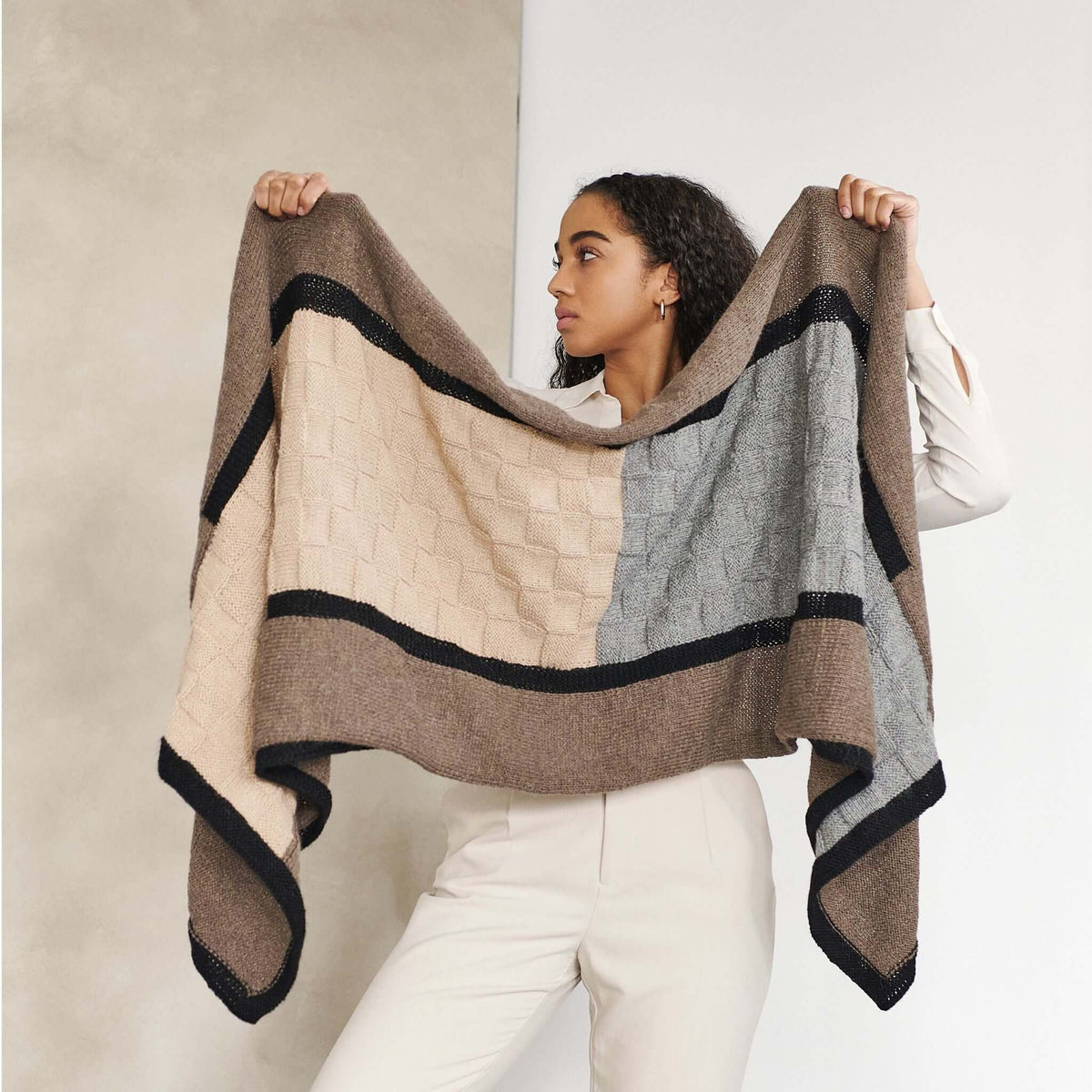 Woman holding the rectangular blanket open to display its color-blocked design and black borders.