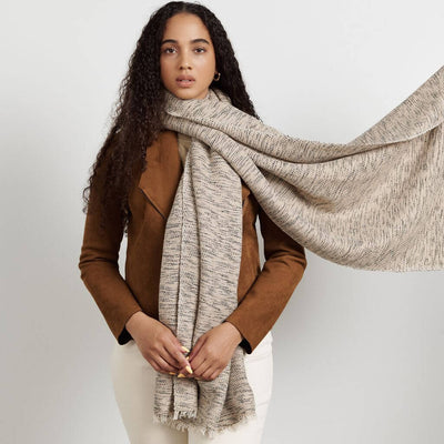 Woman in a brown jacket styling the long fringed scarf around her neck and shoulders.