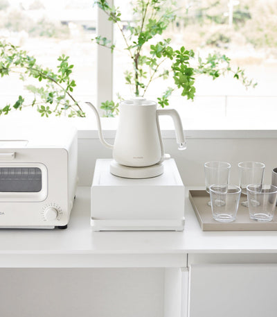 White kitchen setup with a kettle, toaster oven, and glasses on a white countertop.