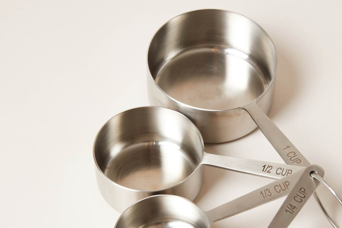 Close-up of stainless steel measuring cups with long flat handles engraved with measurement markings.