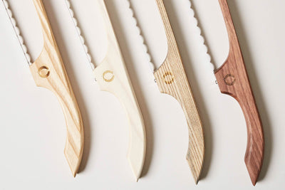 Close-up lineup of four bread bows showing pale maple, cream, textured natural wood, and dark walnut frame finishes.