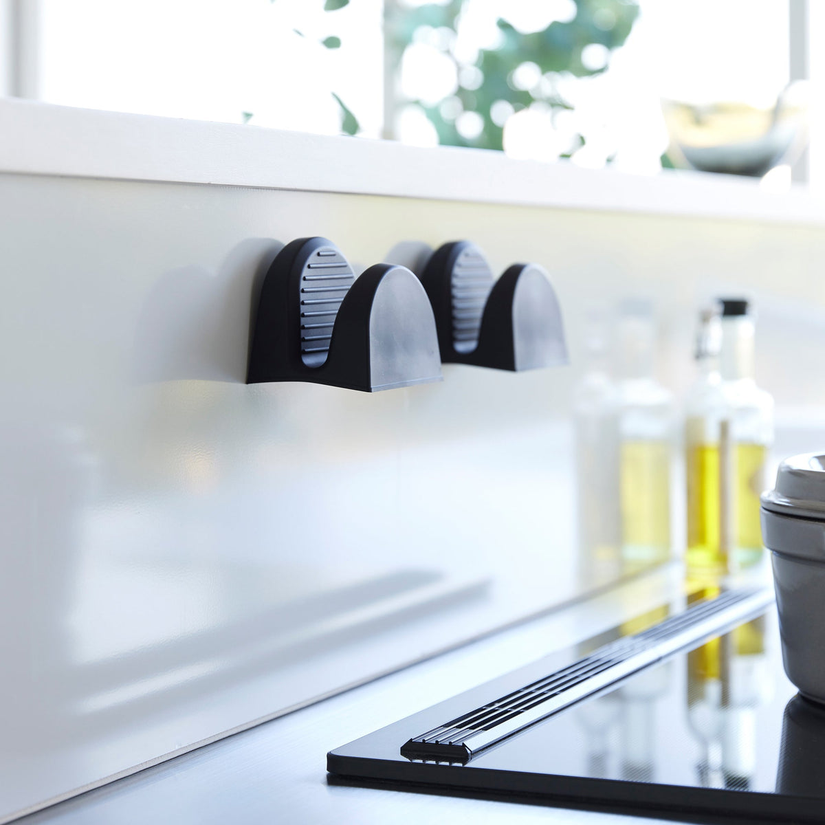 Two black Yamazaki Home Magnetic Pot Holders - Set of 2 - Silicone attached side by side to a pale kitchen backsplash, with their ridged interiors visible.