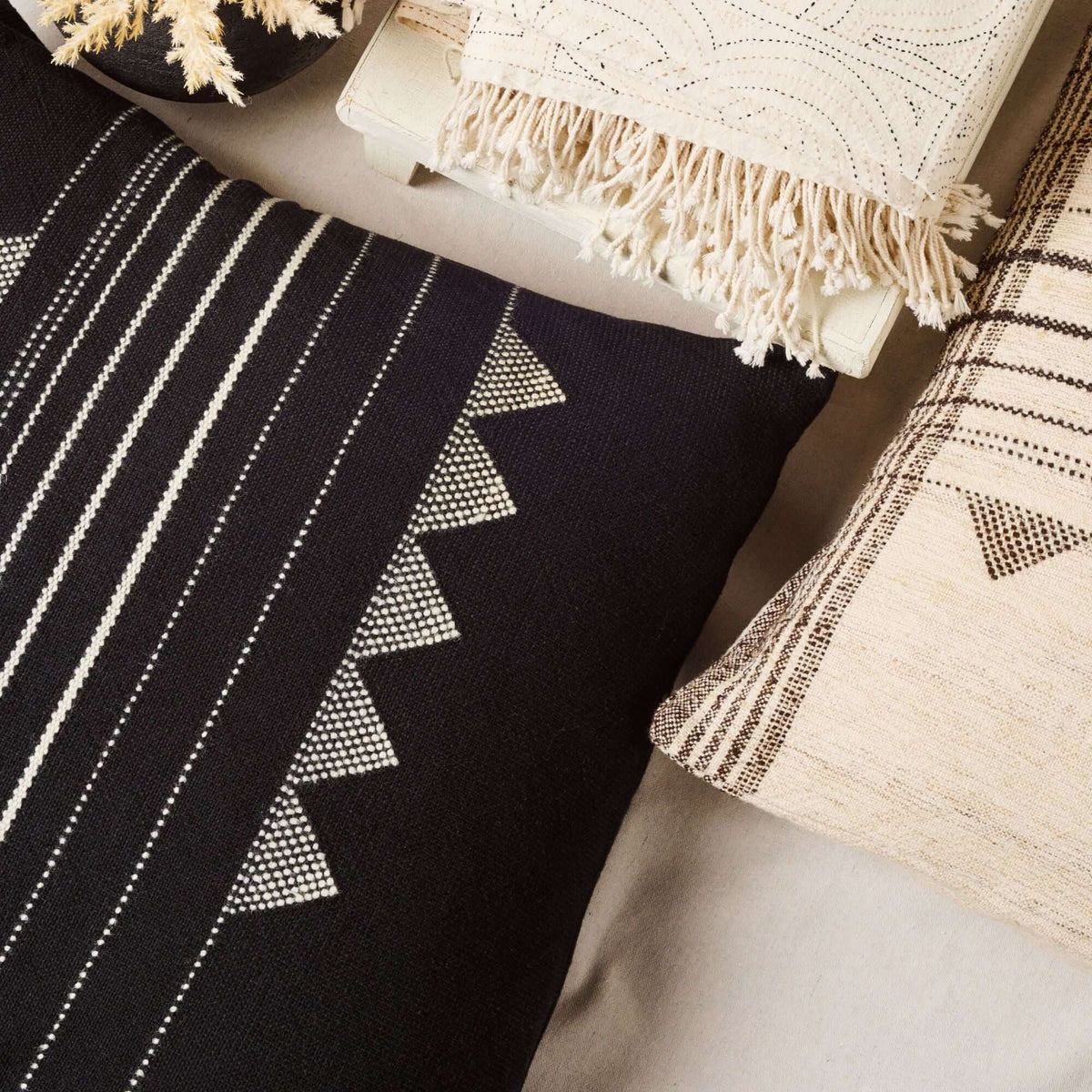 Close lifestyle view of the Kora Black pillow among neutral cushions, showing its ivory stripes and triangular motifs
