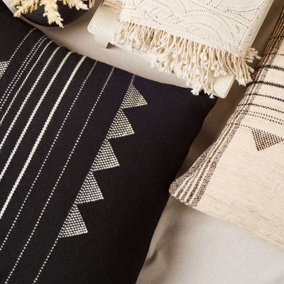 Close lifestyle view of the Kora Black pillow among neutral cushions, showing its ivory stripes and triangular motifs