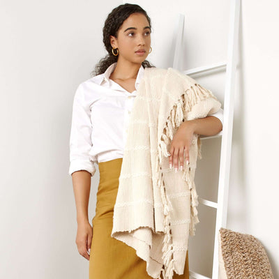 Woman wearing the Sea Shell White textured throw over her shoulders like a shawl, with fringe hanging along one side