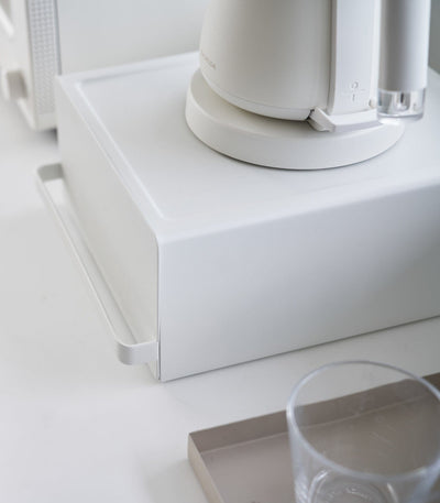 White electronic device on a white surface with a glass of water nearby