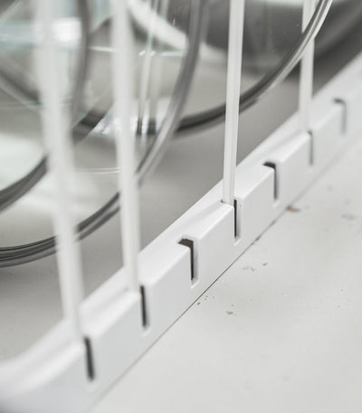 Close-up of the white Yamazaki Home Adjustable Pot Lid Organizer - Steel base, showing divider wires inserted into evenly spaced rectangular slots beneath upright lids.