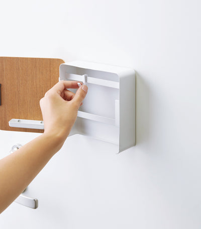 Hand reaching for a white wall-mounted shelf on a white background